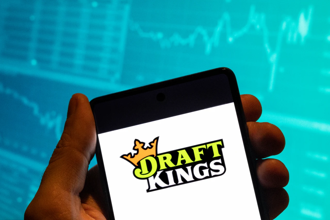 In this photo illustration, the American daily fantasy sports contest and sports betting company DraftKings logo is seen displayed on a smartphone with an economic stock exchange index graph in the background.